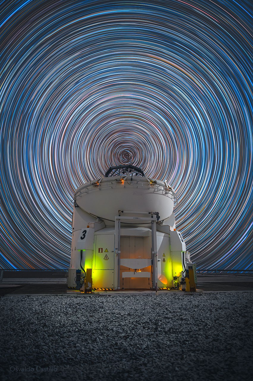 Rastros de estrelas concêntricos ao redor do polo celeste sul sobre o Telescópio Auxiliar AT 3 no Observatório de Paranal, Chile.